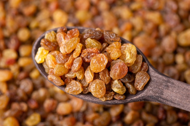 Macro shot of raisins in wooden spoon Tasty sweet raisins background adding raisins to pastry