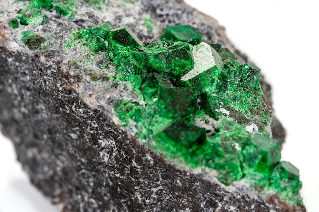 Macro stone garnet mineral Uvarovite in rock on a white background