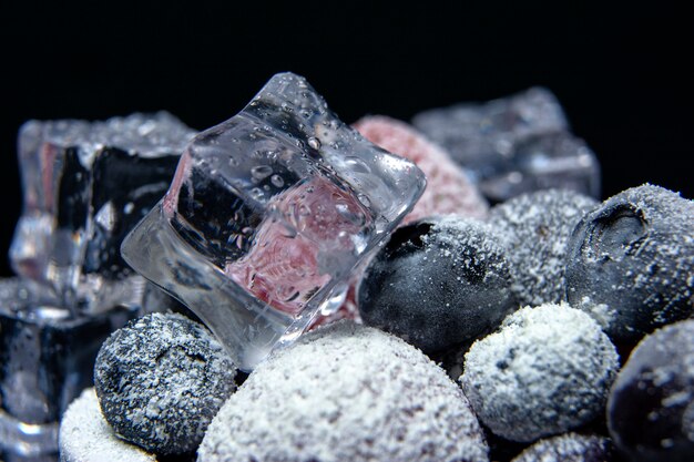 Macro view of frozen berries: strawberry, blueberry with ice cubes on dark background