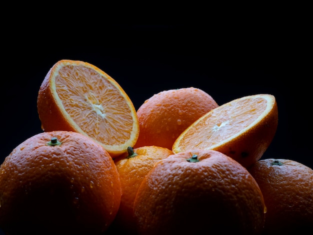 Foto macrofotografie van hele en gesneden sinaasappelen op zwarte achtergrond in studio