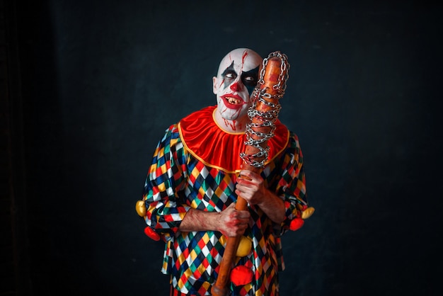 Mad bloody clown with baseball bat. Man with makeup in halloween costume, zombie