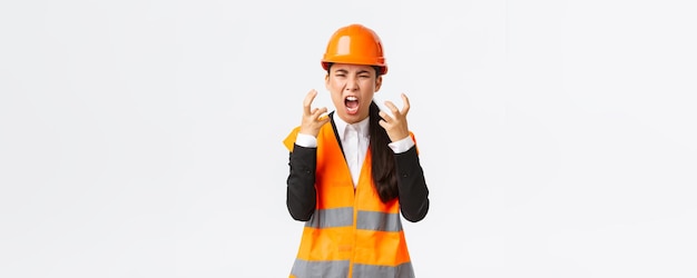Mad and outraged asian female chief engineer construction manager burst in rage losing temper at employees shouting and shaking hands aggressive scream furious as scolding someone