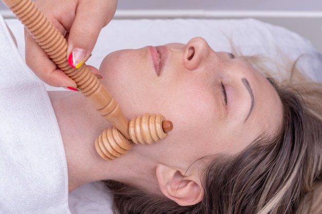 Madero-therapie, ontspannende massage tegen veroudering - Handen die de nek van het meisje masseren met behulp van een natuurlijke houten stimulator. Gezichtsliftmassage, correctie en verwijdering van mimische rimpels