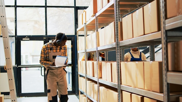 Foto magazijnmedewerker danst en zingt op het werk, vermaakt zich met dansmoves in opslagruimte. jonge volwassene die producten of goederen klaarmaakt in pakketten, kartonnen dozen op rekken. schot uit de hand.