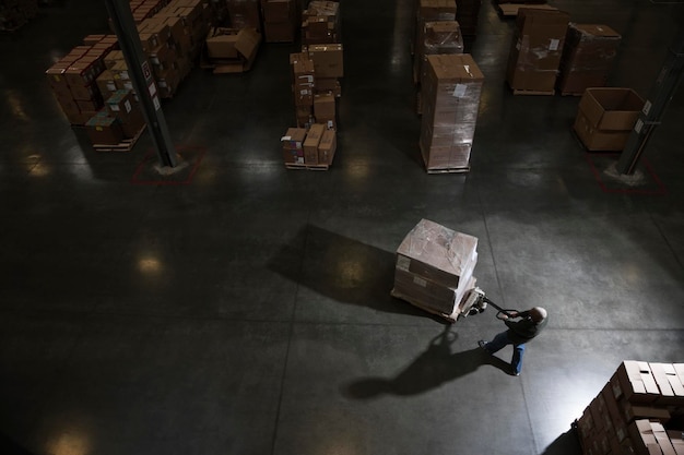 Foto magazijnmedewerker die een handmatige palletkrik gebruikt om enkele producten in een distributiemagazijn te verplaatsen