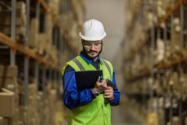 Magazijnmedewerker met harde hoed en bril die naar documenten kijkt