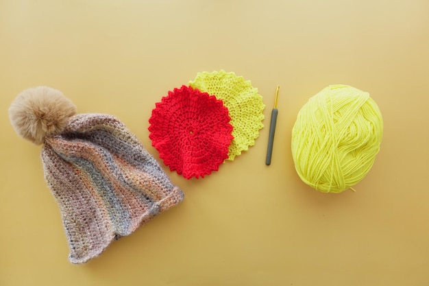 A magenta crocheted cap with woolen yarn and crochet hook displayed on table