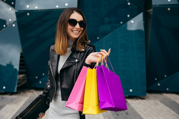 Magere mooie jonge vrouw die met het winkelen zak dichtbij de wandelgalerijshowcase glimlacht