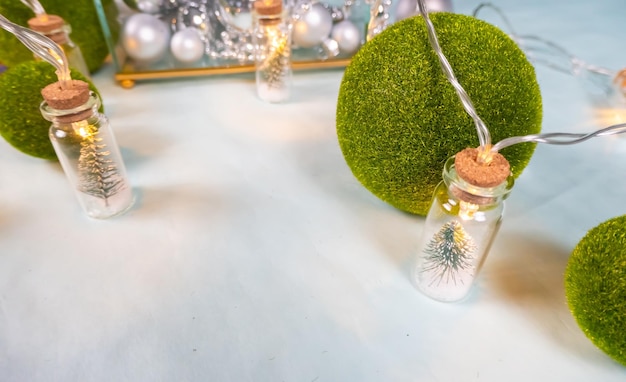 Волшебная гирлянда Игрушечные елки в стеклянных банках и шарики зеленой травы на синем фоне стеклянная шкатулка с серебряными украшениями