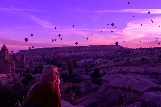 Alba magica a goreme cappadocia turchia. una ragazza in un canyon in abiti tradizionali circondata da palloncini sotto i raggi del sole nascente