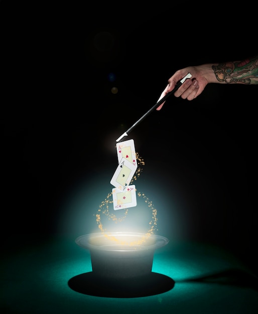 Magician performing playing card trick over the top hat with glowing lights against black background