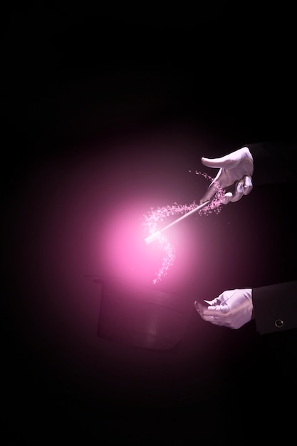 Photo magician's hands performing magic trick over a magical top hat against black background