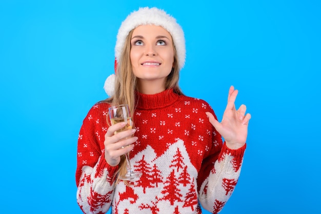 Magie is bijna hier! portret van gelukkige glimlachende vrolijke mooie vrouw die een wens met gekruiste vingers doet en een glas champagne houdt, dat op heldere blauwe achtergrond wordt geïsoleerd