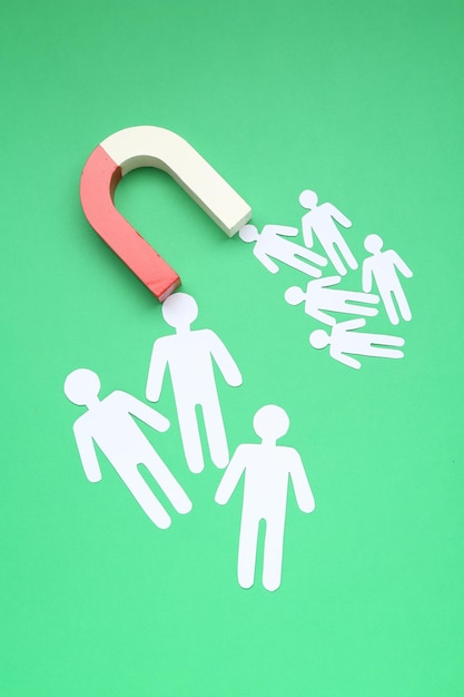 Magnet attracting paper human figures on green background flat lay
