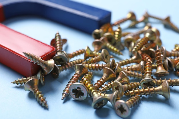 Magnet attracting screws on light blue background closeup