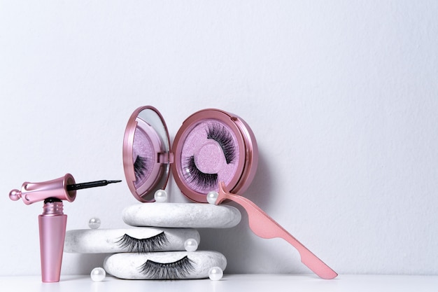 Magnetische nep kunstwimpers in roze spiegelkit, eyeliner, pincet op witte achtergrond. Home wimper extensie, cosmetologie tool concept, schoonheidsbehandeling, verbetering van het fysieke uiterlijk