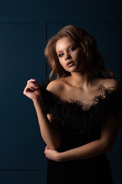 Magnificent blonde woman wearing black dress with naked shoulders, posing in the shadows