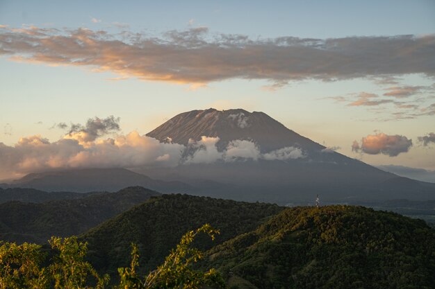 Magnificent landscape of grassy hills and majestic volcano surrounded by clouds stock photo