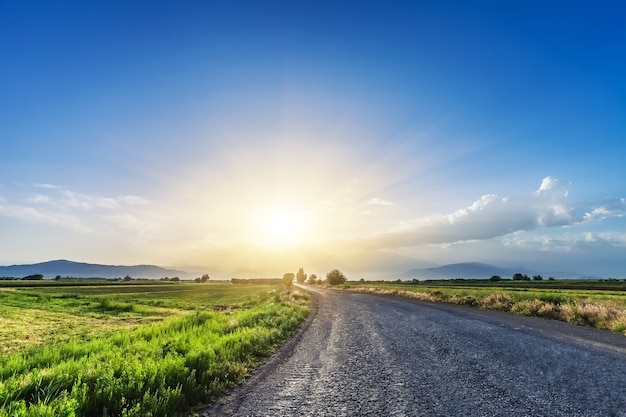 Magnificent landscape of road on meadow on background of beautiful sunset sky with clouds