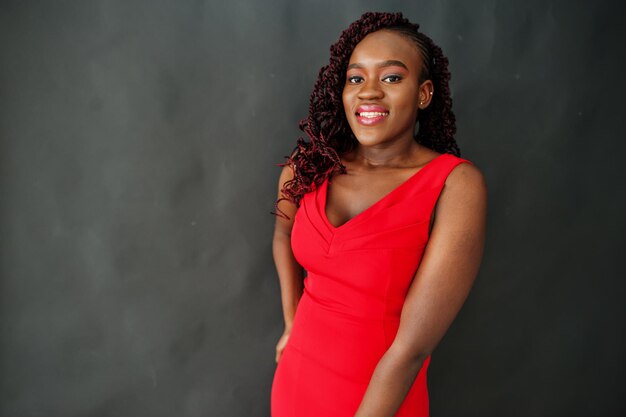 Magnificent young african woman in luxurious red dress against black background. Beauty, fashion.