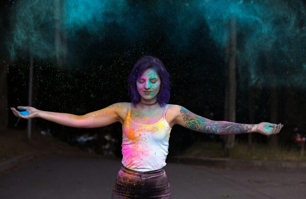 Magnificent young woman with purple hair tossing up colorful Holi powder