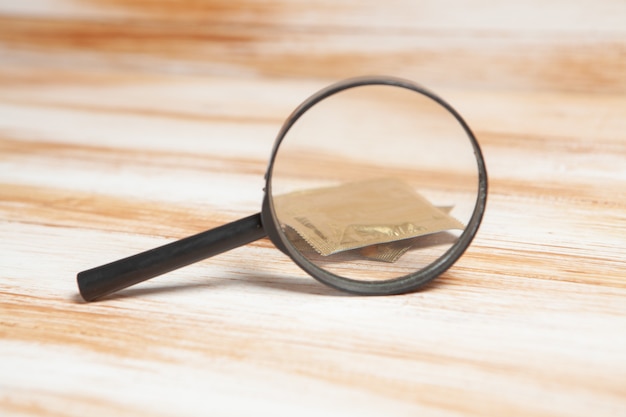 Magnifier and condom on wooden table