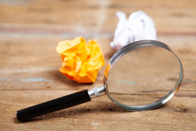 Magnifier and crumpled papers on a wooden table. concept search for an idea