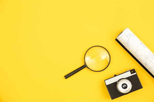 Magnifier map and camera on yellow background flat lay