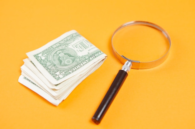 Magnifier and money on a yellow surface