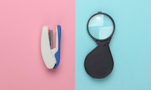 Magnifier and stapler on a pink-blue pastel.