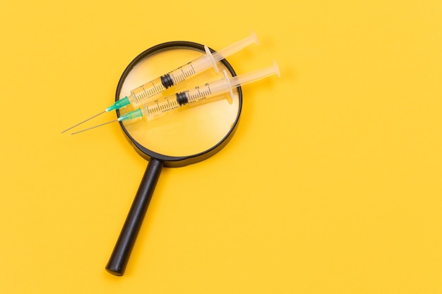 A magnifier with medical syringe on yellow table