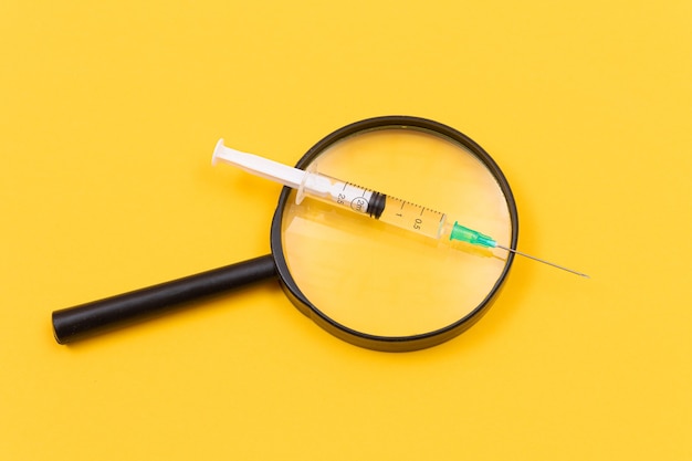 A magnifier with medical syringe on yellow table