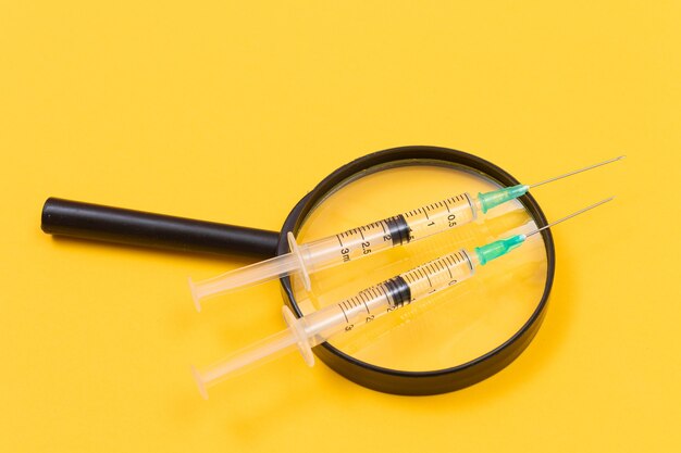 A magnifier with medical syringe on yellow table