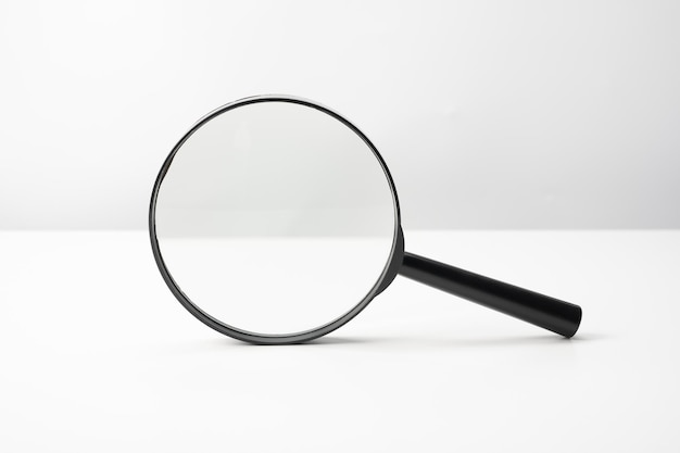 Увеличительное стекло черного цвета на белом столе Исследования в поисках или расследовании чего-либо, вид спереди Увеличительное стекло