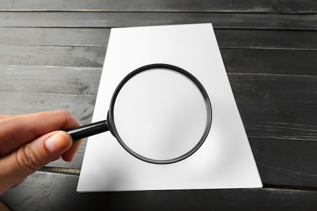 Photo magnifying glass and blank paper on wooden table