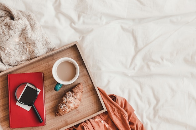 Magnifying glass and book near breakfast food on bed