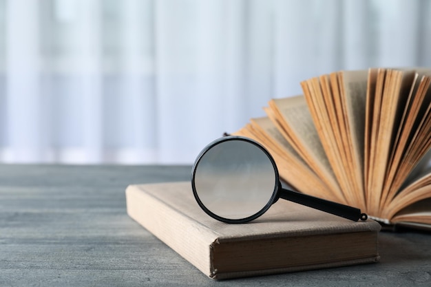 Magnifying glass and books on wooden table on light background space for text