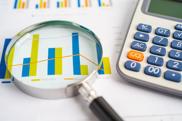 Magnifying glass and calculator on charts graphs paper.\
financial development, banking account, statistics, investment\
analytic research data economy, stock exchange trading, business\
office concept.