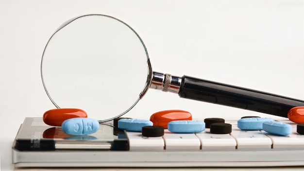 Photo a magnifying glass on a calculator with tablets on a white background