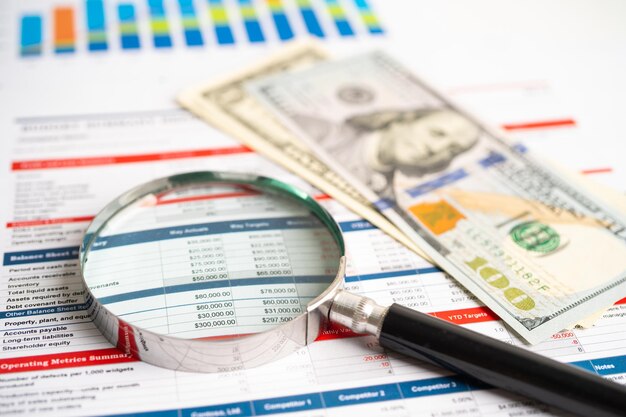 Magnifying glass on charts graphs spreadsheet paper with US dollar banknotes Financial development Banking Account Statistics Investment Analytic research data economy