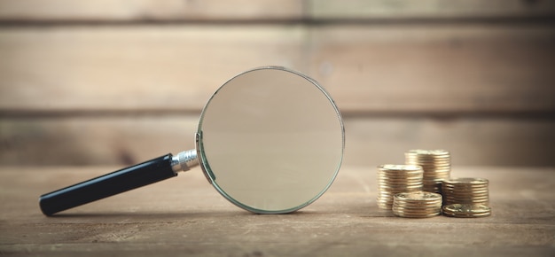 Magnifying glass and coins on wooden table.