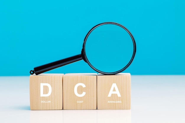 Photo magnifying glass and dca word on a wooden cube in idea dollar cost averaging investment strategy saving stock or savings on a monthly quarterly basis