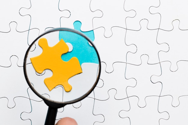 Magnifying glass focusing on yellow puzzle piece over white puzzle piece background