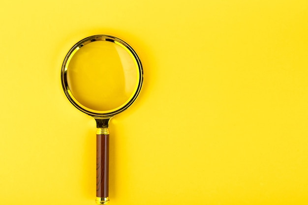 Photo magnifying glass in a gold frame on a yellow wall. copy space.