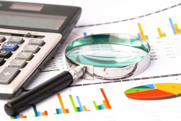 Magnifying glass on graphs spreadsheet paper with calculator.