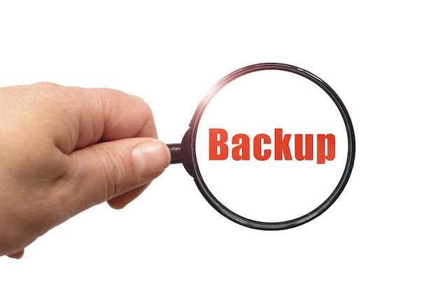 Lente d'ingrandimento in mano e una parola di backup sul bianco.