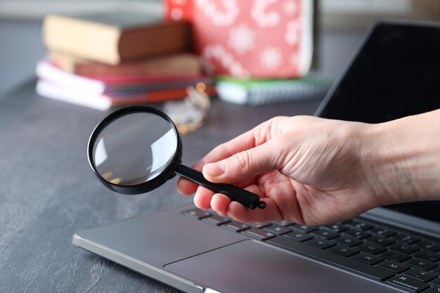 Photo magnifying glass in hand and laptop on wooden background