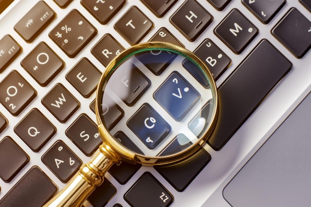 a magnifying glass lies on the keyboard of a modern laptop