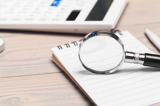 Magnifying glass and notebook on wooden table