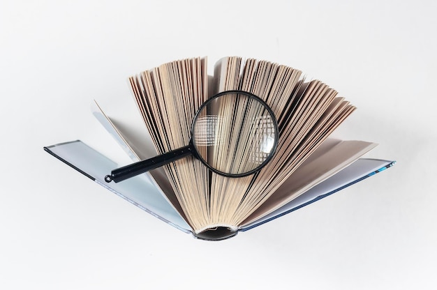 Magnifying glass over open paper book with pages concept of academic research search and studying